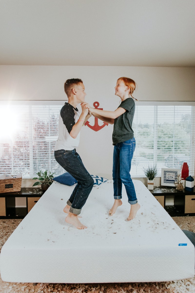 boy and girl jumping on white bed mattress inside room