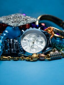 Reloj de pulsera plateado y accesorios sobre superficie azul.