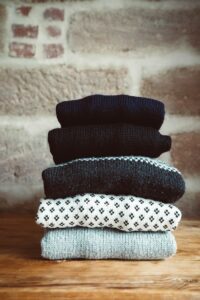 a stack of sweaters sitting on top of a wooden table, knitwear