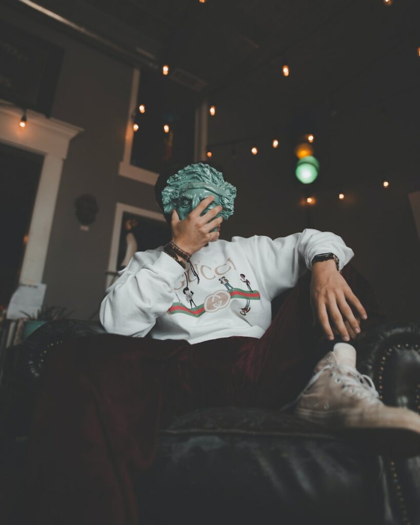 man sitting on leather armchair while holding Statue of Liberty mask