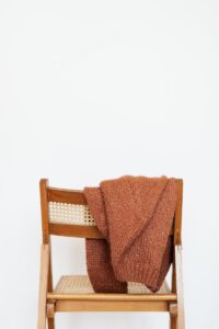 Brown coarse wool sweater hung on back of wooden chair